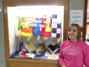Senior Chylie Hopkins stands next to a display of quilts. 